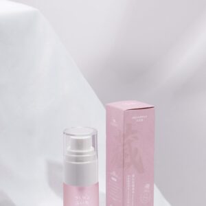 Sophisticated pink skincare serum bottle and box on white fabric backdrop.