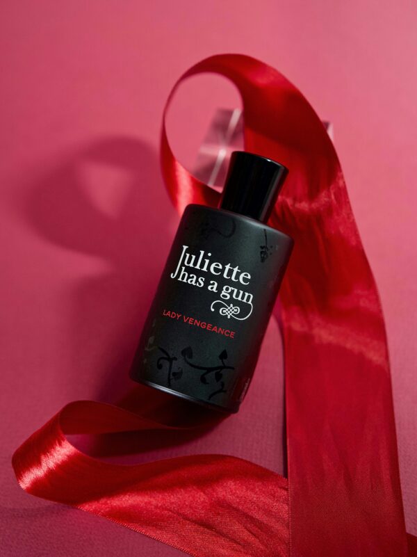 Sophisticated perfume bottle with a red ribbon on a pink background, highlighting elegance and luxury.